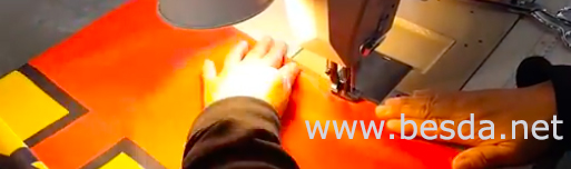Sewing machine stitching an orange printed flag panel in a flag factory